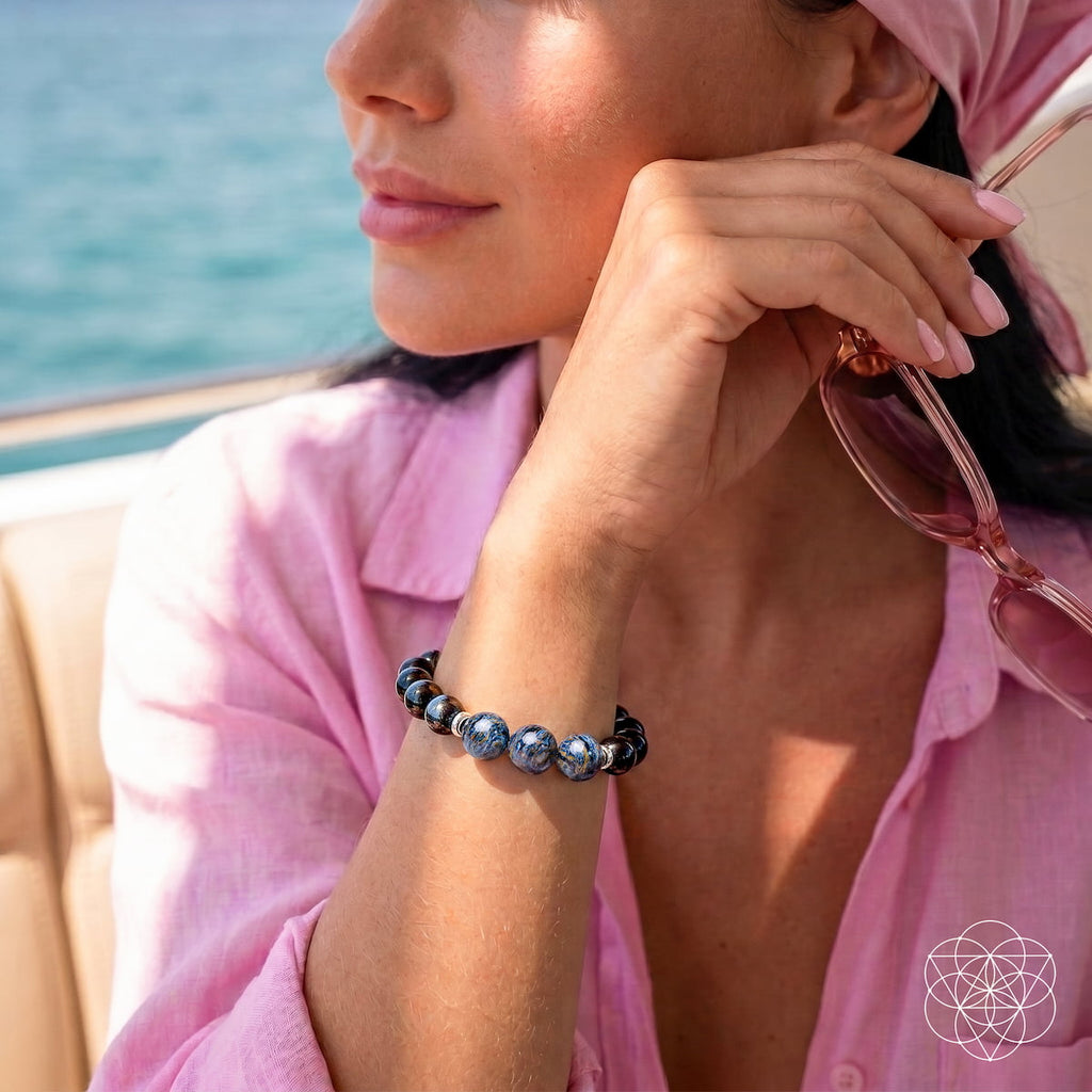 Woman in a pink shirt wearing a blue pietersite and dark obsidian bracelet while holding sunglasses near her face.
