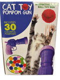 Boxed cat toy pom pom gun set with a purple ball gun, a red pom pom, and a circular inset showing 30 colorful pom poms. The packaging features a cat reaching for a red pom pom and bold text reading 'CAT TOY POMPOM GUN' and 'INCLUDES 30 COLORFUL POMPOMS'.