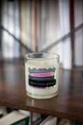 Candle in a glass jar with a colorful label on a wooden surface.