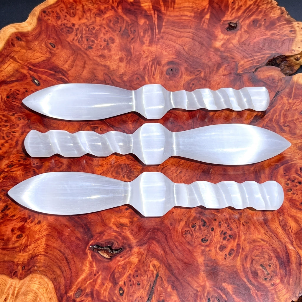 Three white satin spar decorative daggers with carved spiral handles displayed on reddish wood
