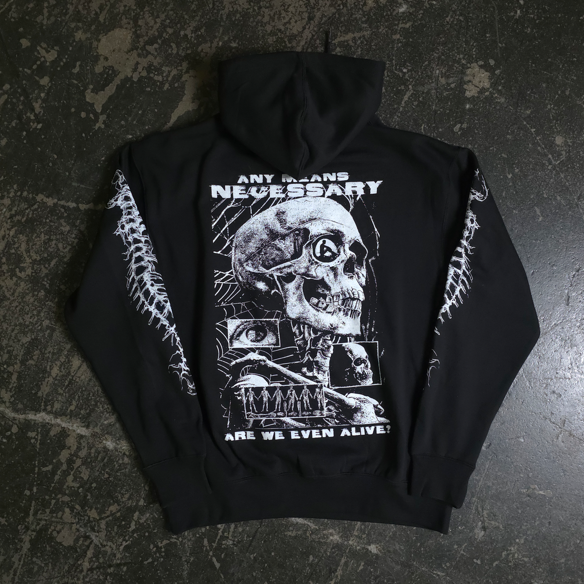 Black hoodie with a graphic design on the back featuring a skull and text, laid flat on a textured surface.