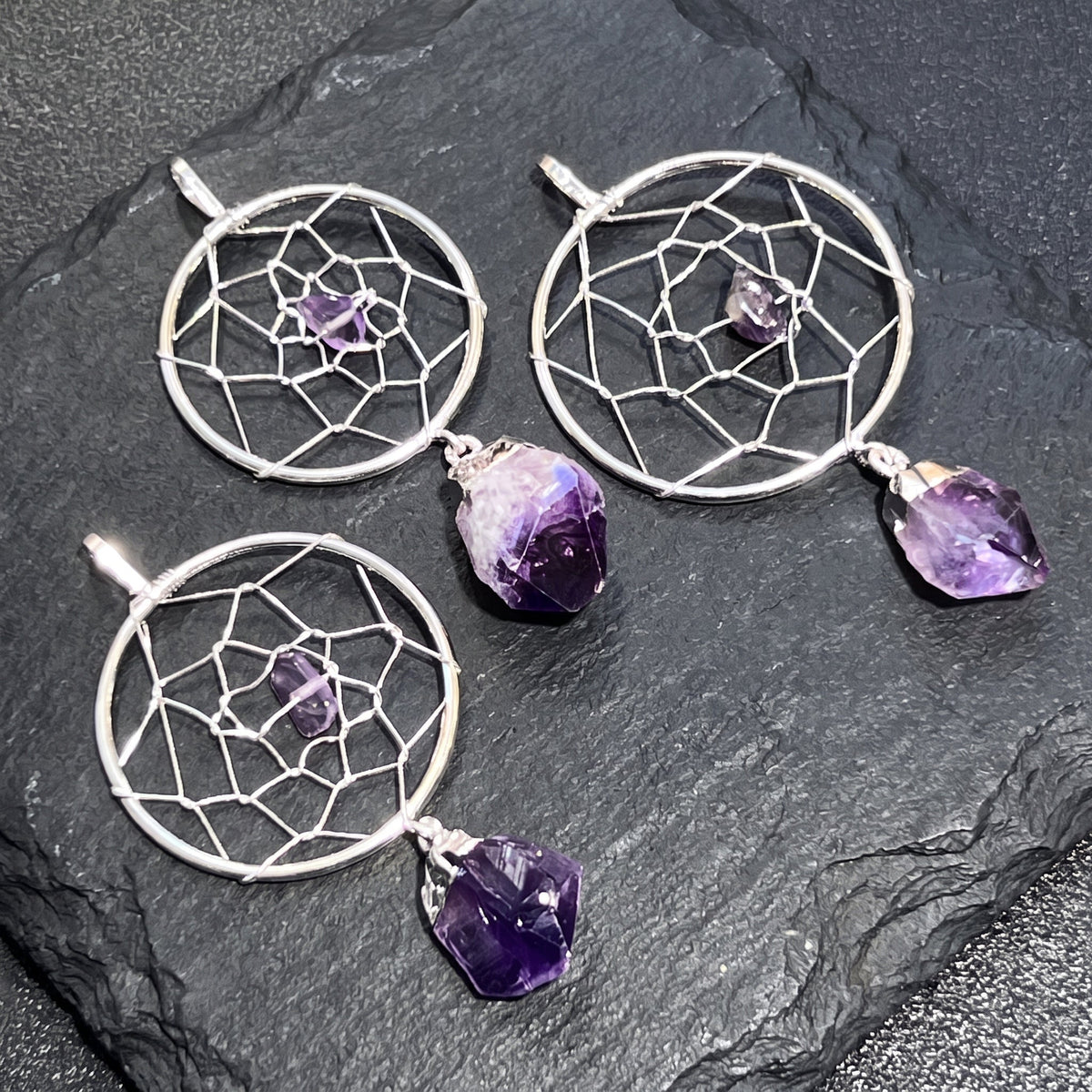Amethyst dreamcatcher pendants arranged on dark slate with small purple center stones and larger crystal drops