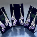  Amethyst triple crystal dangle earrings with silver-plated chains displayed on three black stands.