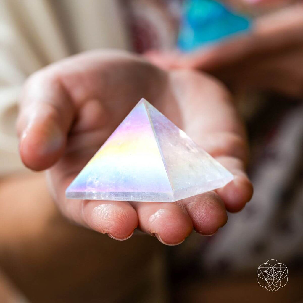 Pale Angel Aura quartz pyramid with rainbow reflections resting in an open hand.
