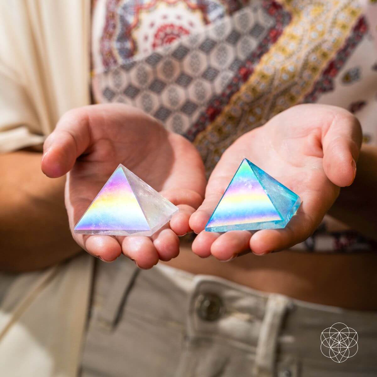 Person holding a pale Angel Aura quartz pyramid and a blue Aqua Aura quartz pyramid in separate hands.
