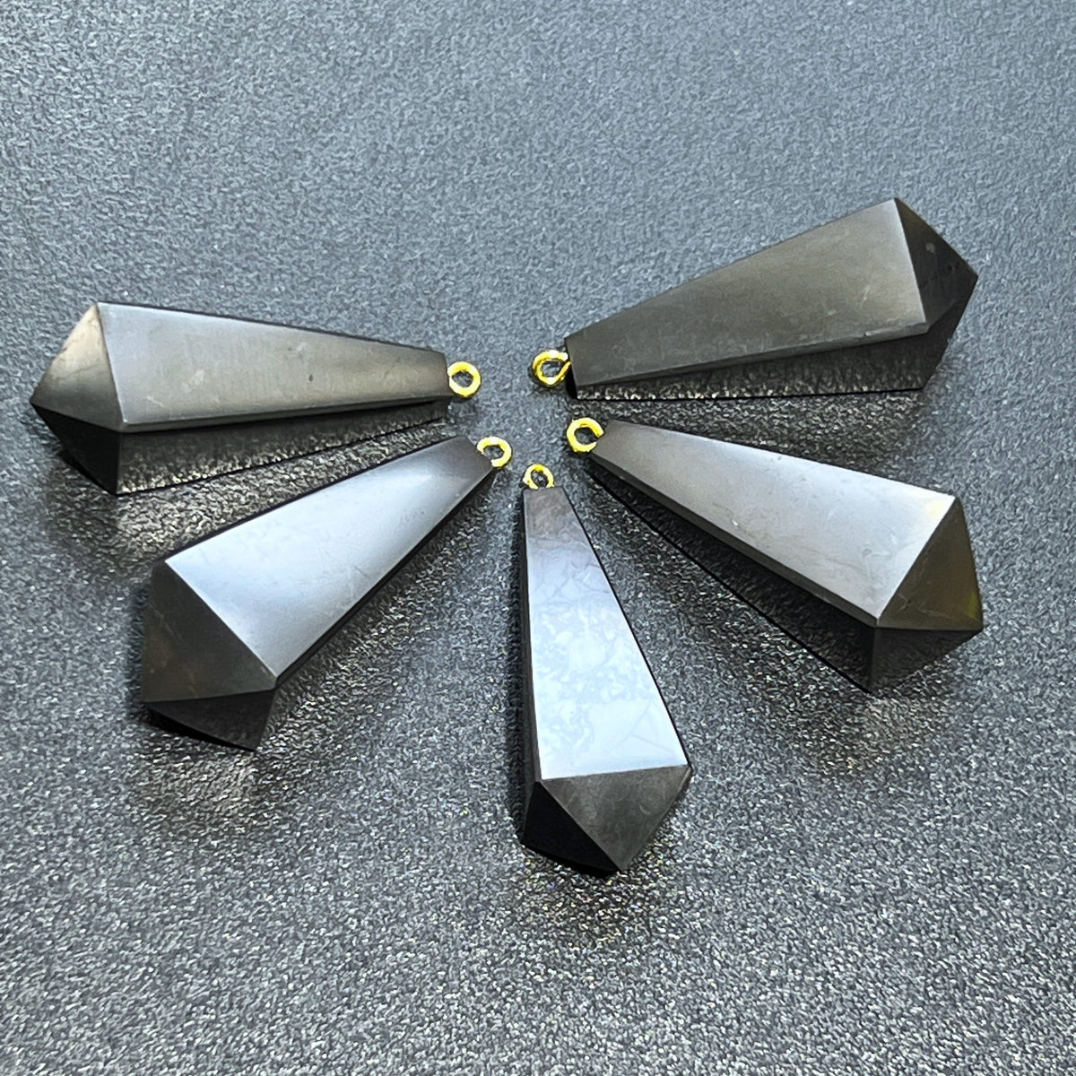 Black shungite point pendants arranged in a fan with hanging loops toward the center and pointed ends facing outward.

