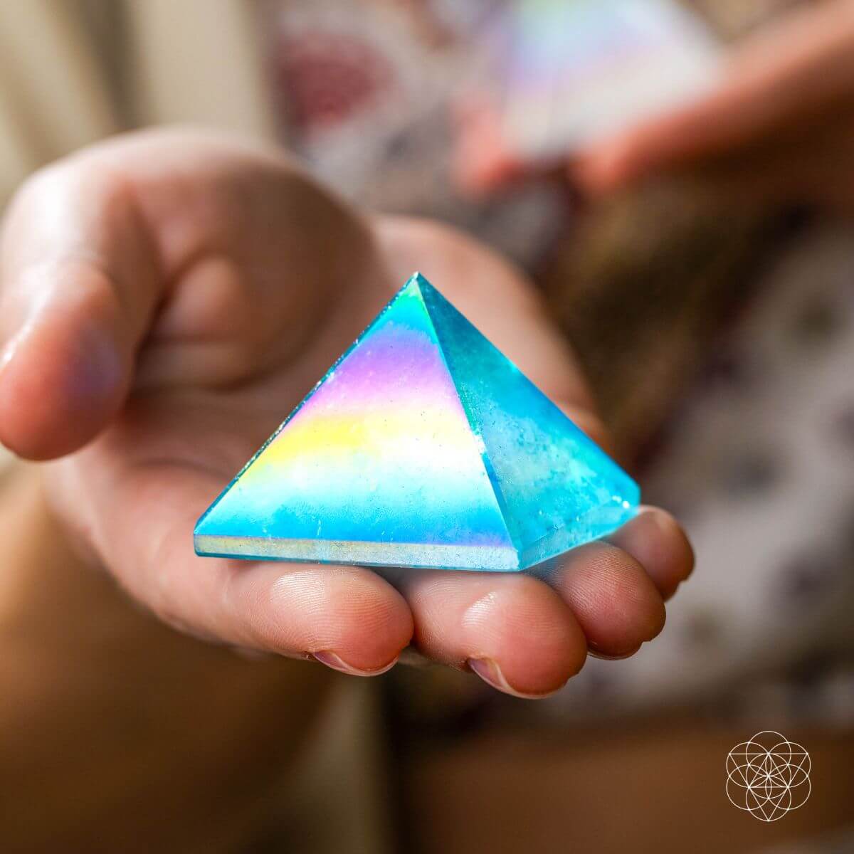 Blue Aqua Aura quartz pyramid with an iridescent rainbow sheen held in an open palm.
