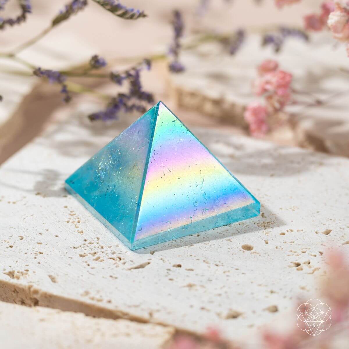 Blue Aqua Aura quartz pyramid with rainbow reflections and visible internal markings on a stone slab.
