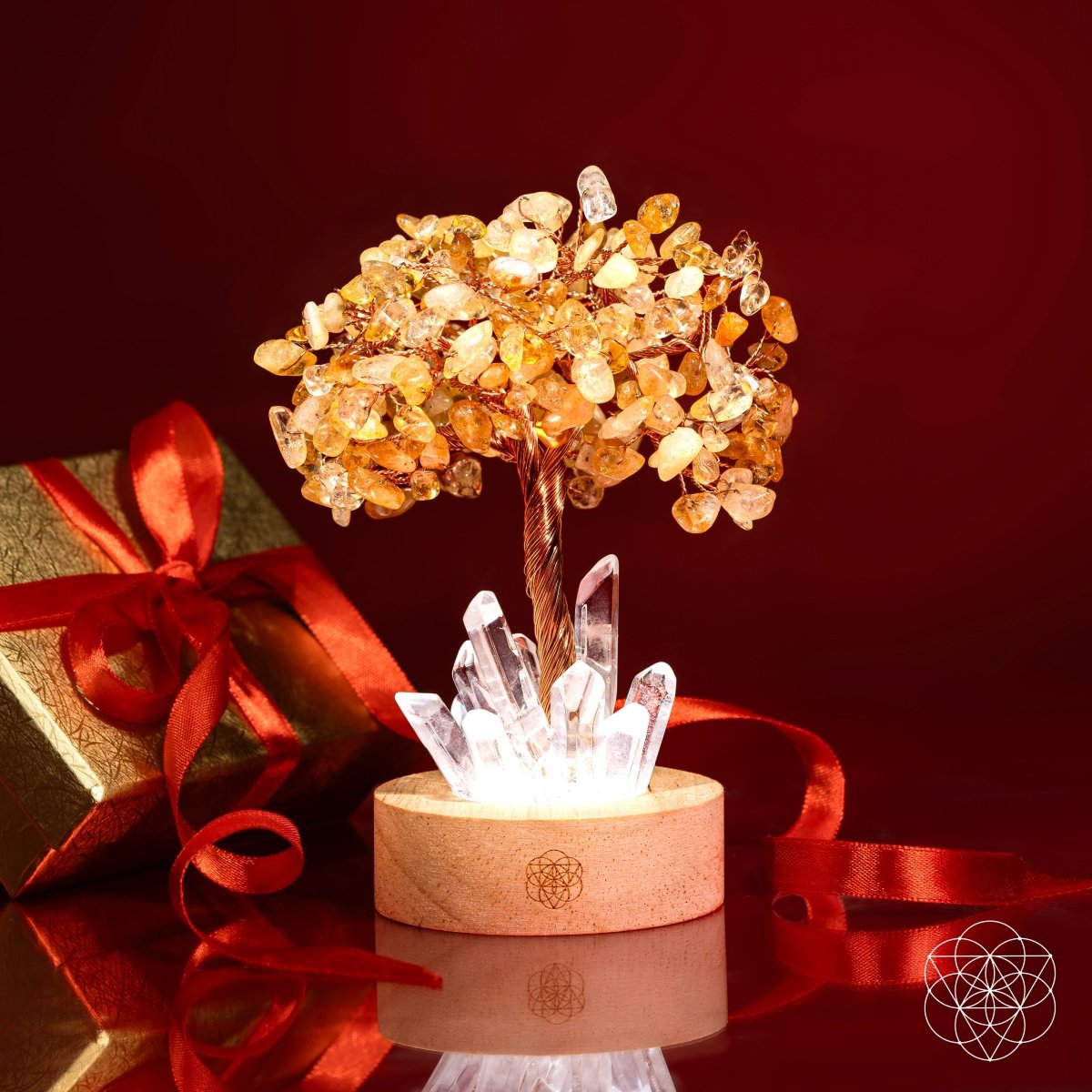 Citrine crystal tree lamp illuminated beside a gold gift box and red ribbon against a red background.
