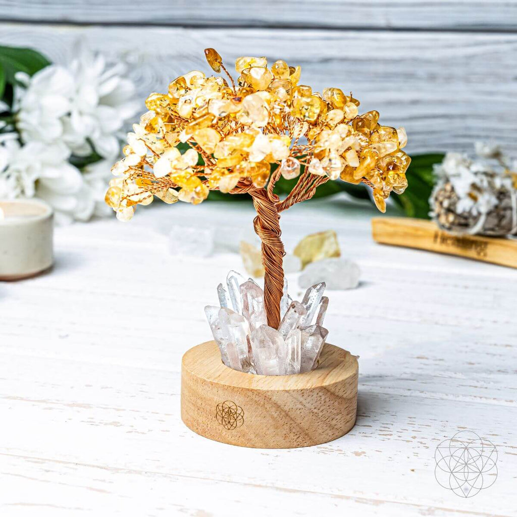 Citrine stone-chip tree with twisted copper branches and clear quartz points on a wooden lamp base in daylight.

