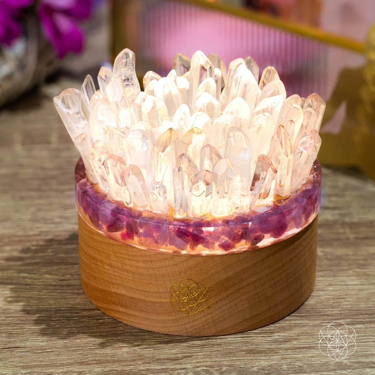 Clear quartz and pink tourmaline lamp illuminated on a wooden tabletop, showing its crown-like crystal arrangement.
