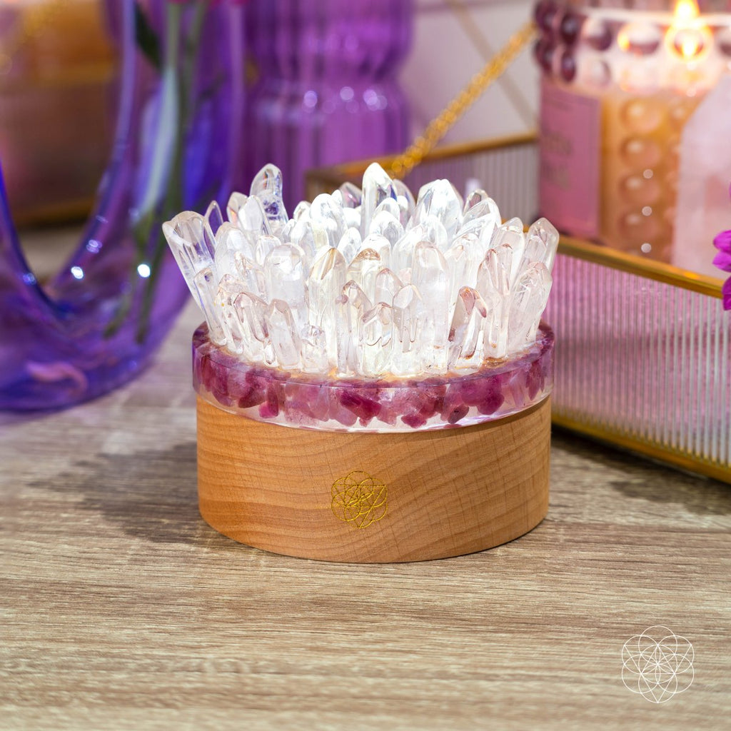 Clear quartz point lamp with pink tourmaline accents and a wooden base displayed beside a purple vase.
