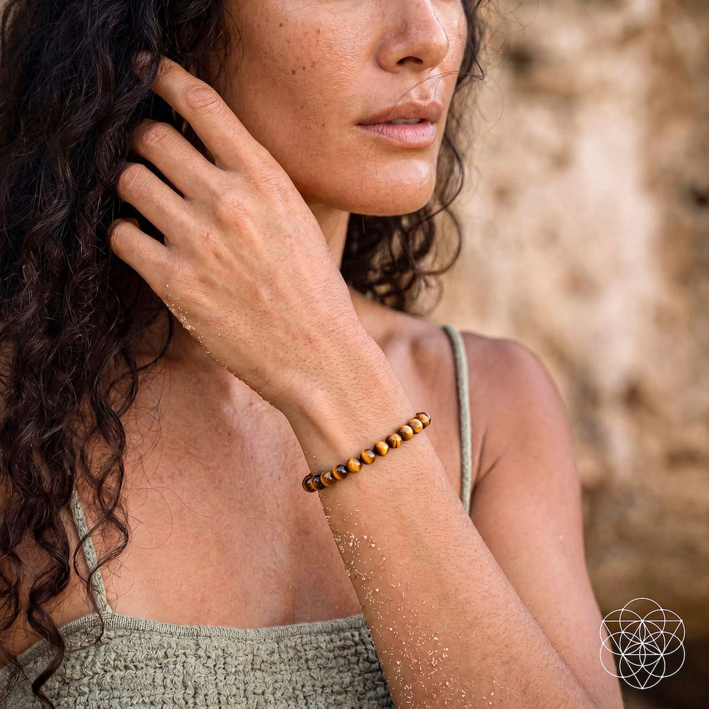 A woman outdoors wearing a beaded bracelet with dark brown and amber-orange beads. The photo is a close-up of her face, hand, and arm, with a blurred natural stone wall in the background.