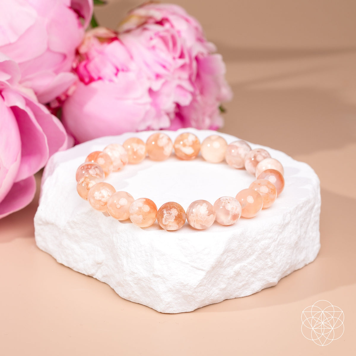 Peach Sakura Flower Agate bead bracelet on a white stone display beside pink flowers.
