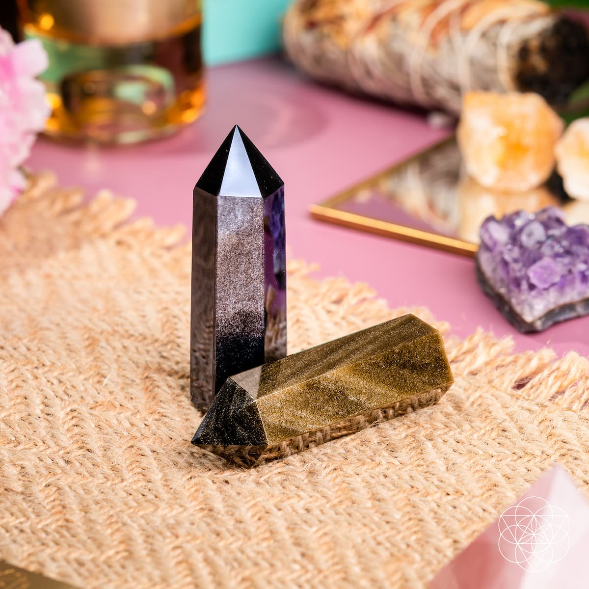 Silver sheen obsidian point upright beside a reclining gold sheen point on a woven mat.
