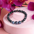 Pietersite and silver sheen obsidian bracelet on a pink display, with blue patterned focal beads and magenta orchids.
