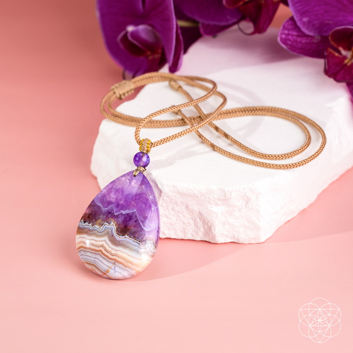 Close-up of the polished purple and cream-banded teardrop pendant with a purple bead and gold-colored cord.