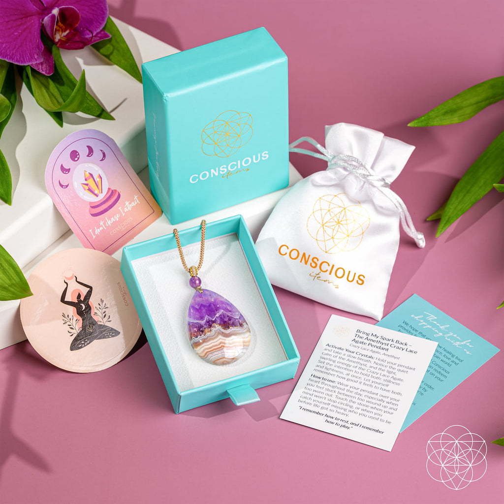 Amethyst and crazy lace agate pendant in a turquoise Conscious Items box beside a white pouch and printed cards.