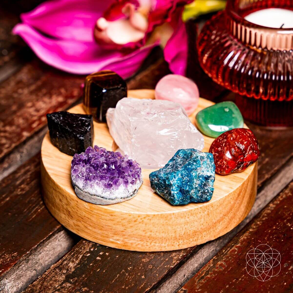 Eight-stone crystal display on a round wooden lamp base, with clear quartz in the center beside flowers and a candle.
