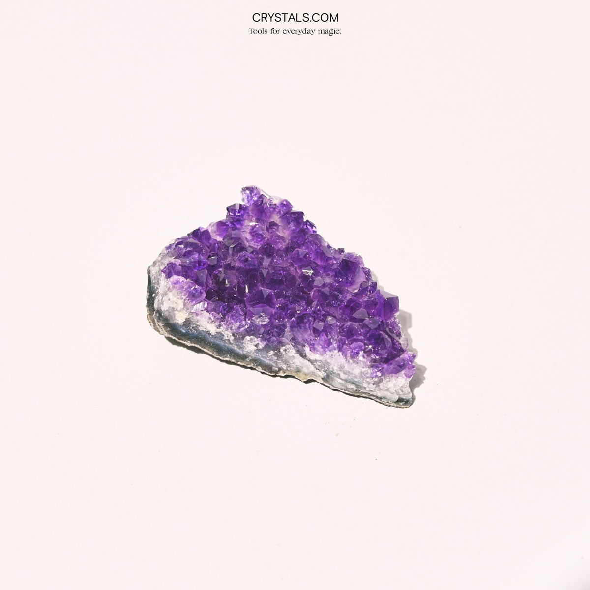 Elongated purple amethyst cluster with a pale quartz border and dark stone base on pink.
