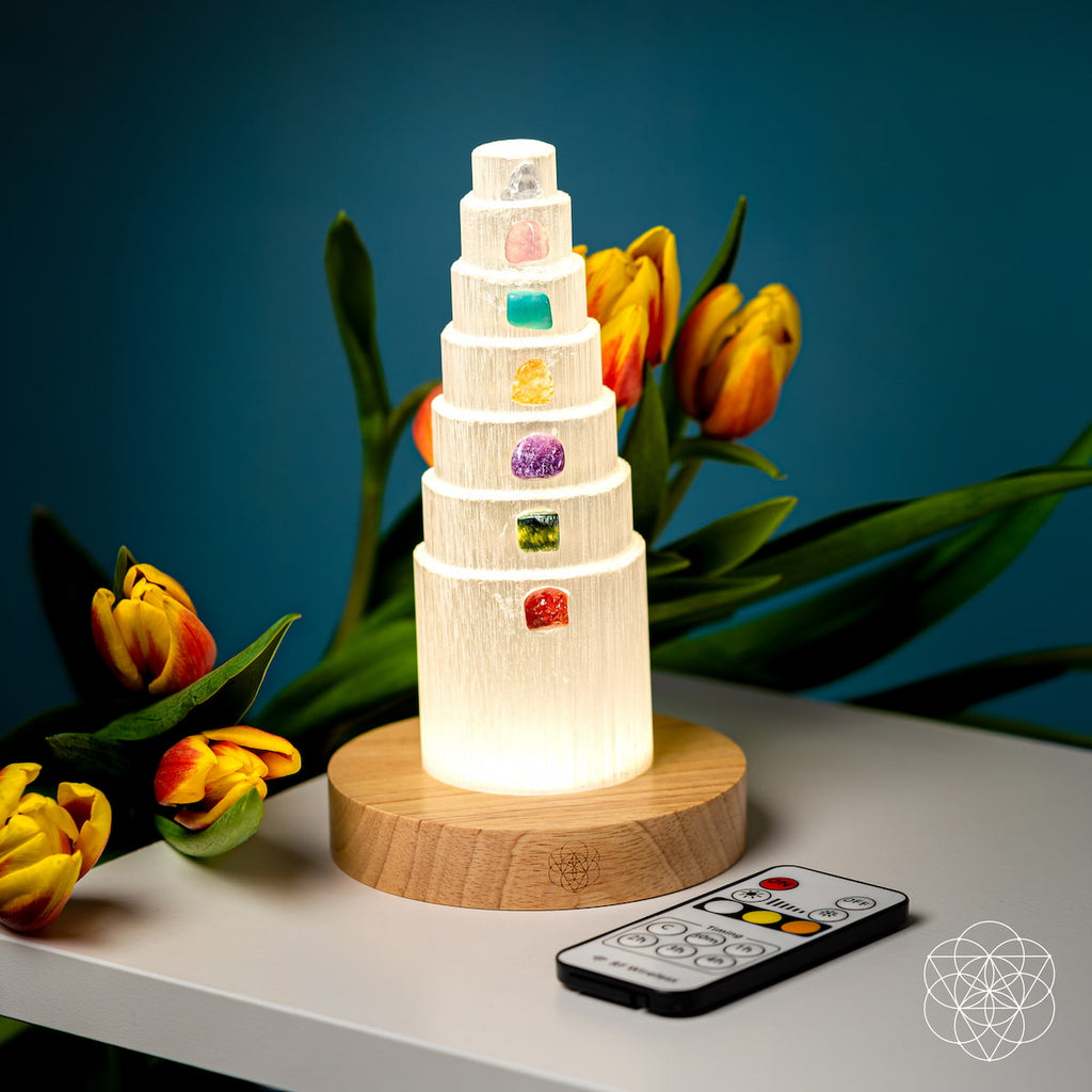 Glowing selenite crystal lamp and remote control on a white table with tulips against a teal background.
