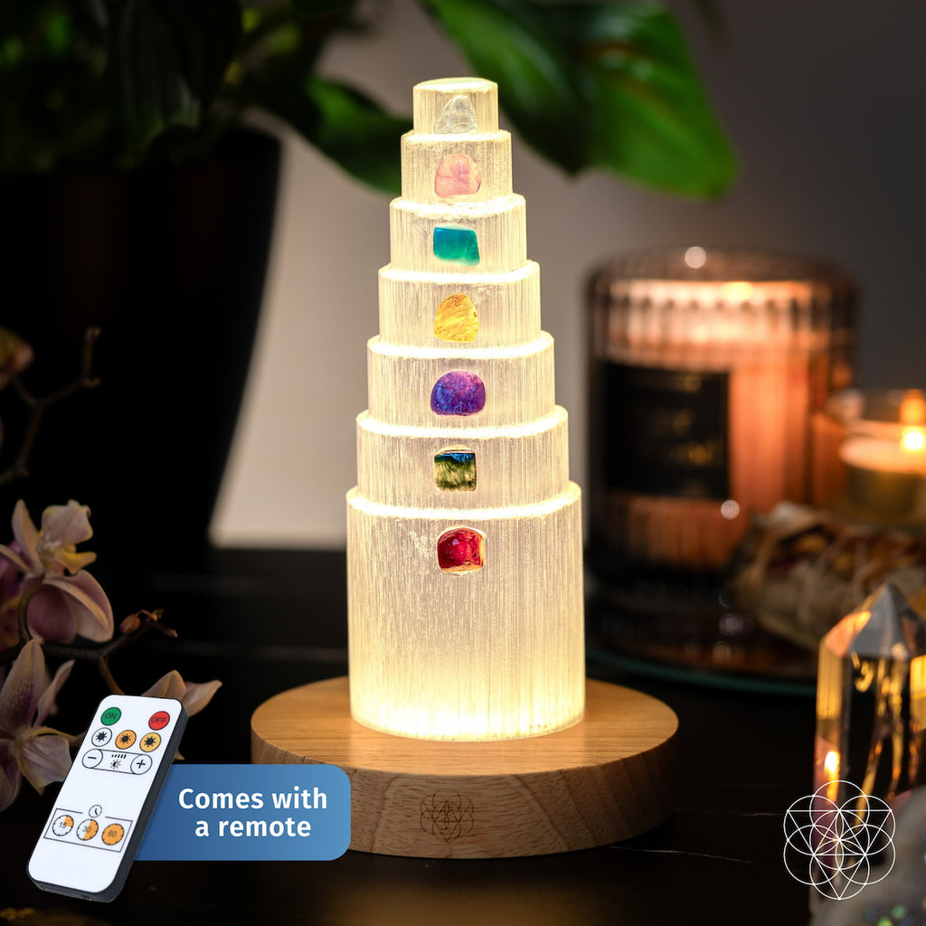 Glowing tiered selenite lamp with seven colorful stones on a wooden base, shown with its remote control.