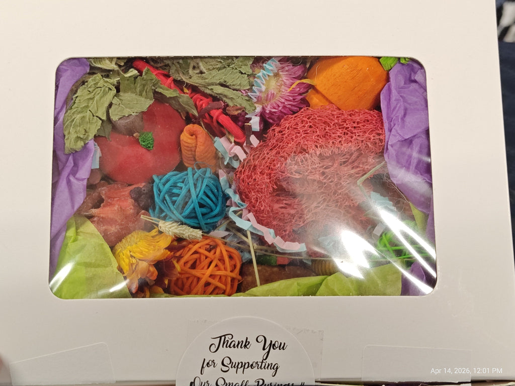 A white gift box with a clear window showing a colorful assortment of handmade crafts, yarn balls, dried leaves, and purple tissue paper. A handwritten note at the bottom reads 'Thank You for Supporting Our One-Of-Kind.