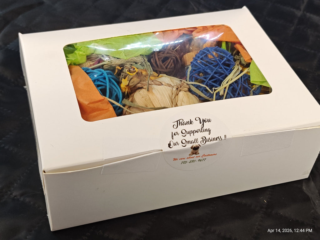 A white cardboard gift box with a clear plastic window showing colorful dried botanicals and blue yarn balls inside, photographed on a dark textured surface. A printed thank-you note is visible on the front.