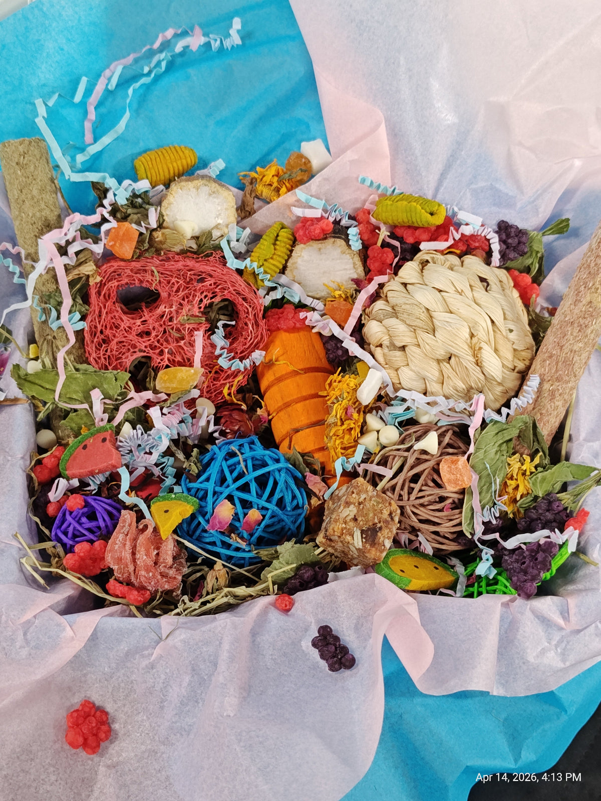 A colorful pet enrichment toy bundle filled with various chew toys, balls, and treats, wrapped in white tissue paper and a bright blue paper liner.