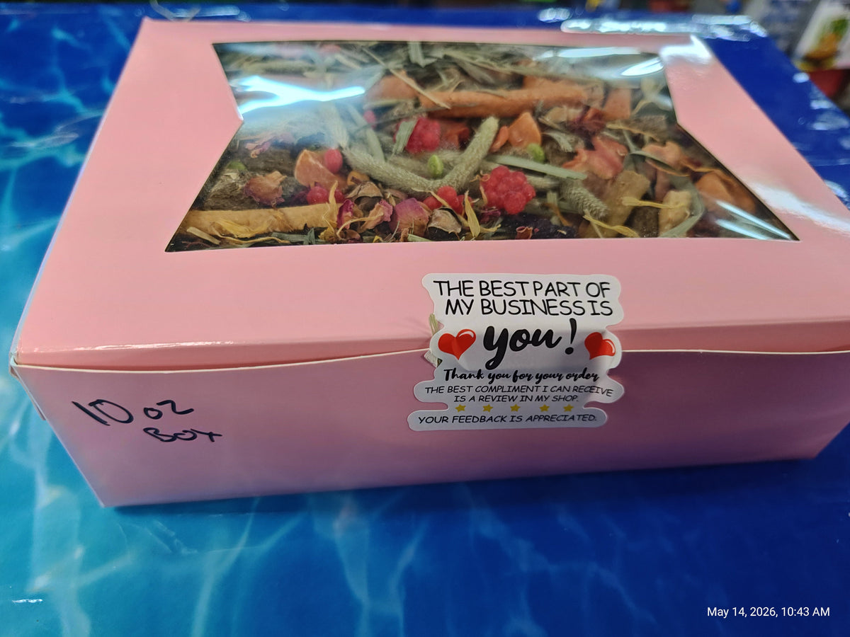 Pink box of tea with a window, containing dried herbs, on a blue surface.