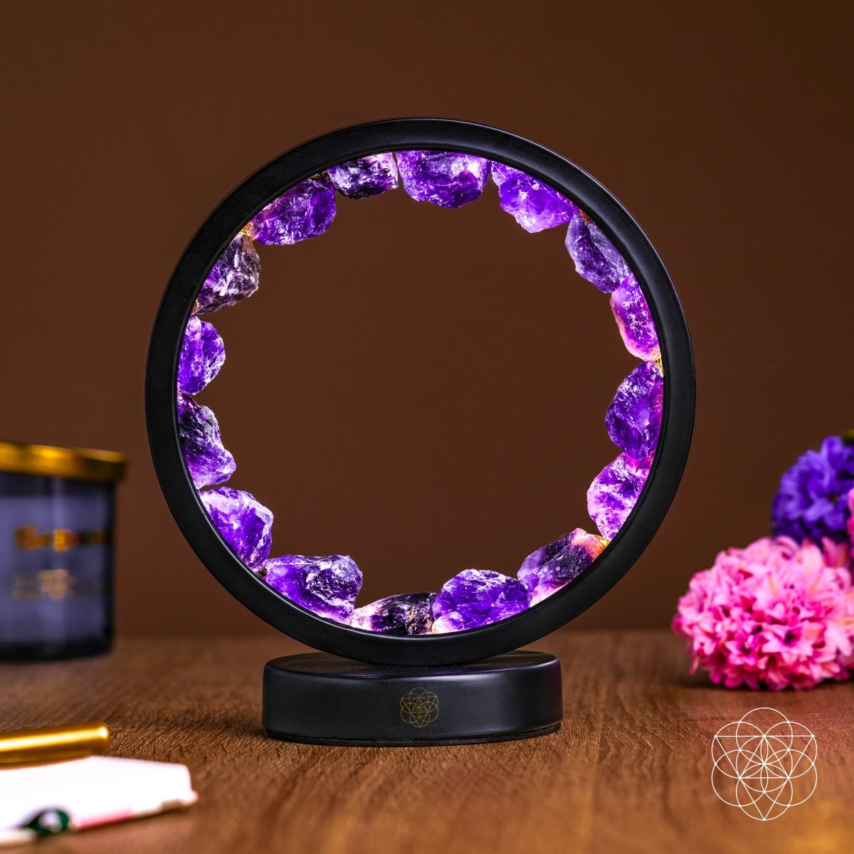Illuminated amethyst halo lamp with rough purple stones in a black circular frame on a wooden tabletop.
