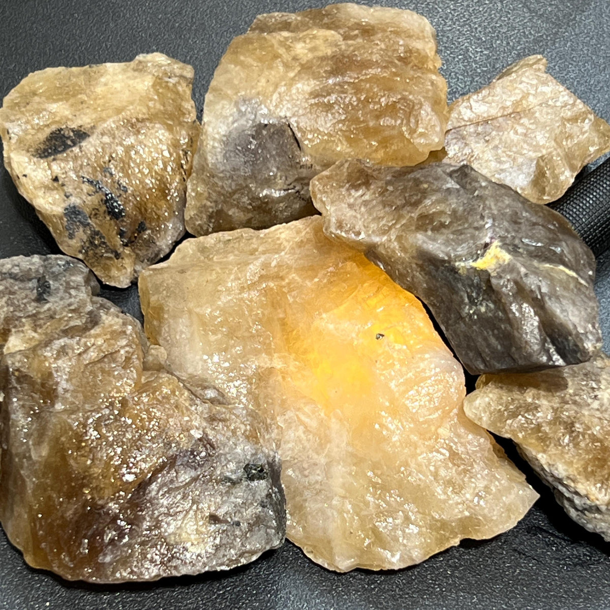 Large rough citrine stones with golden-yellow and smoky areas arranged on a dark textured surface.
