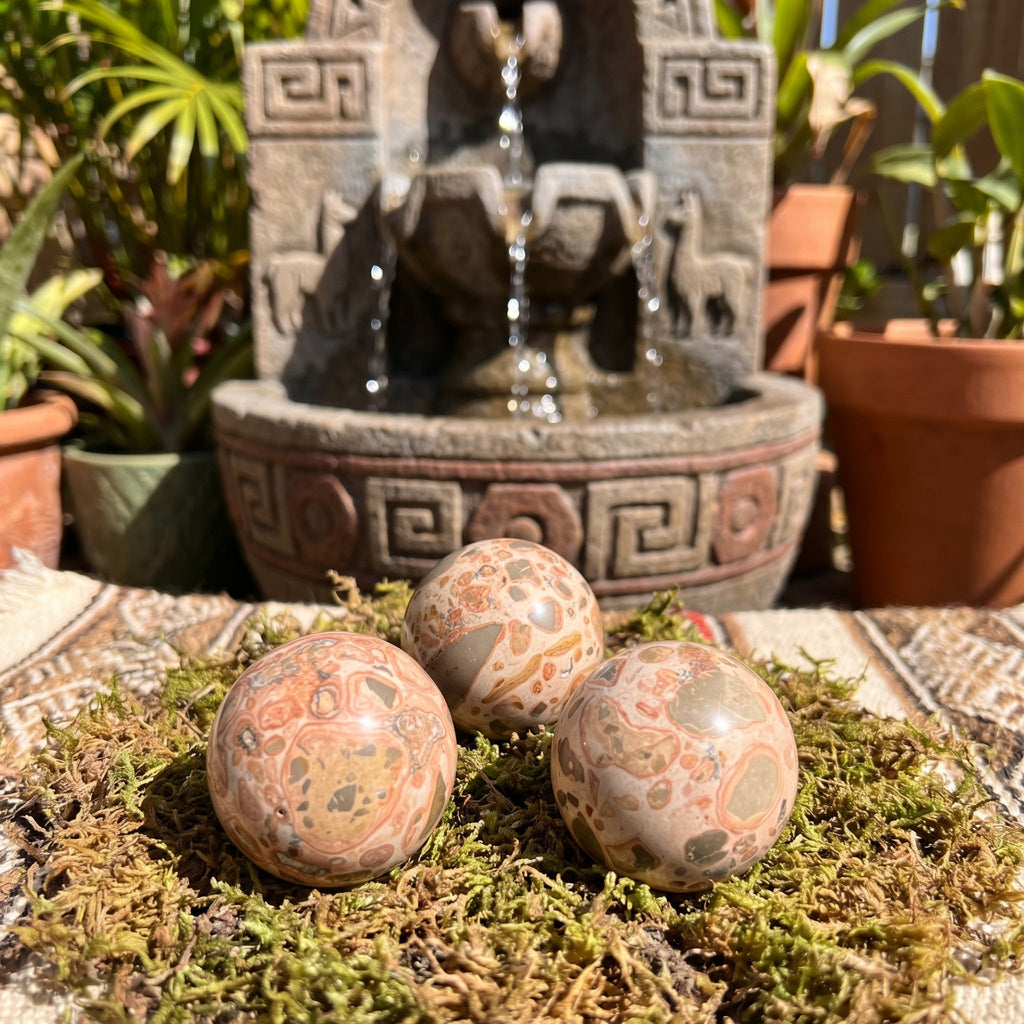 Three leopardite stone spheres arranged on moss in front of a garden fountain.