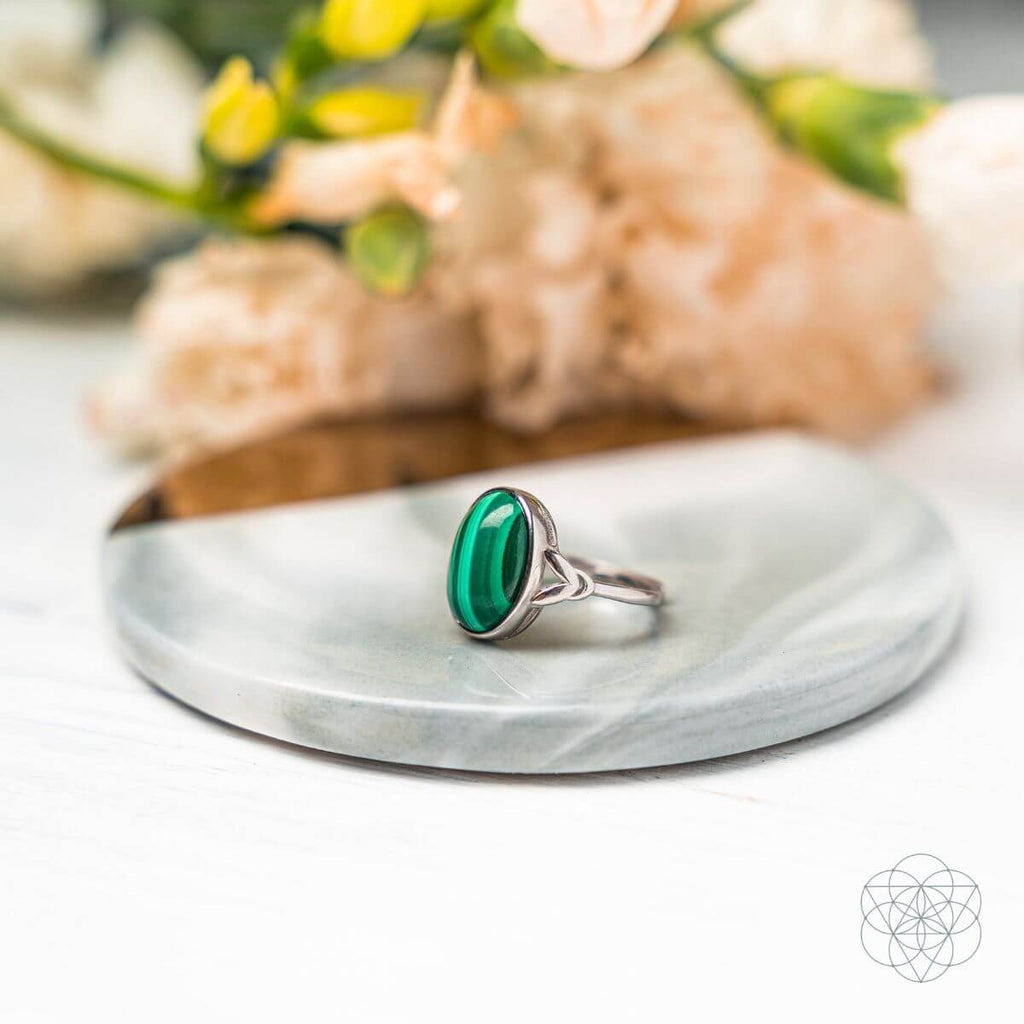 Malachite ring with a silver-colored band and openwork shoulders on a round mirrored tray.
