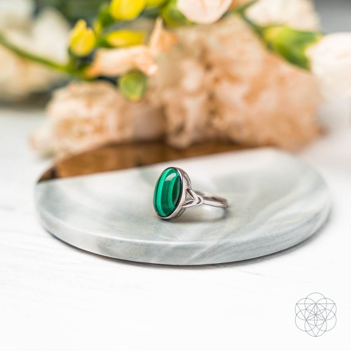 Malachite ring with a silver-colored band and openwork shoulders on a round mirrored tray.
