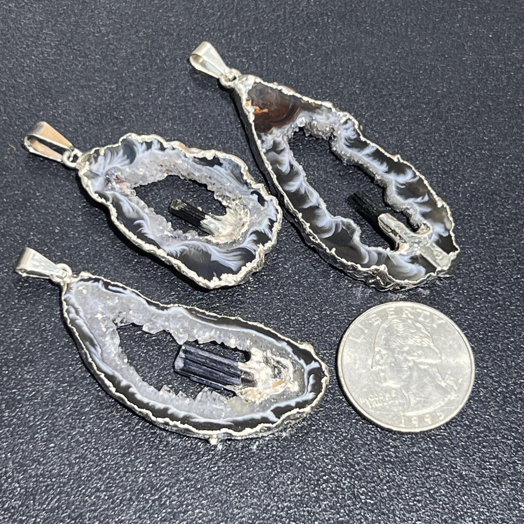 Three Oco geode and black tourmaline pendants with silver-plated edges beside a quarter for scale