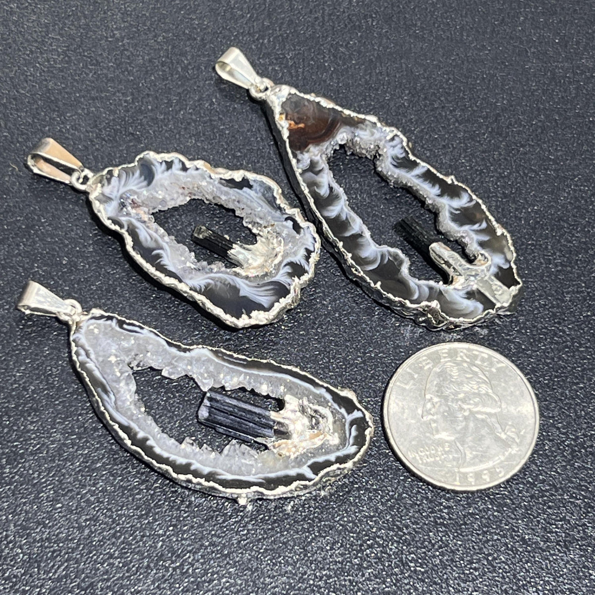 Three Oco geode and black tourmaline pendants with silver-plated edges beside a quarter for scale