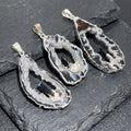 Three silver-plated Oco geode pendants with white druzy interiors, dark banding and black tourmaline accents on slate