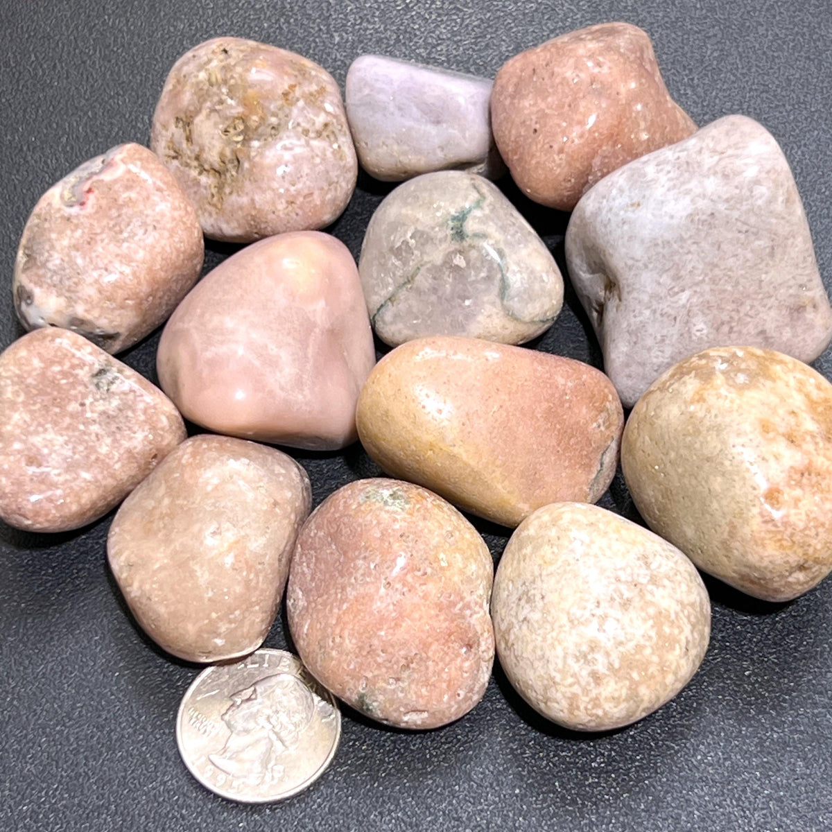 Pink amethyst tumbled stones with varied natural markings beside a quarter for scale