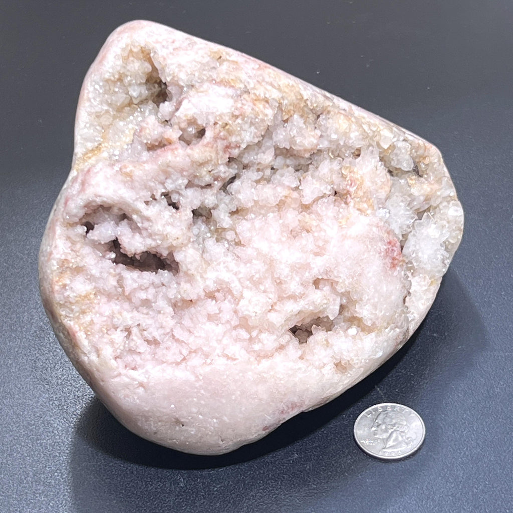 Pink amethyst druzy freeform on a dark surface beside a quarter for scale