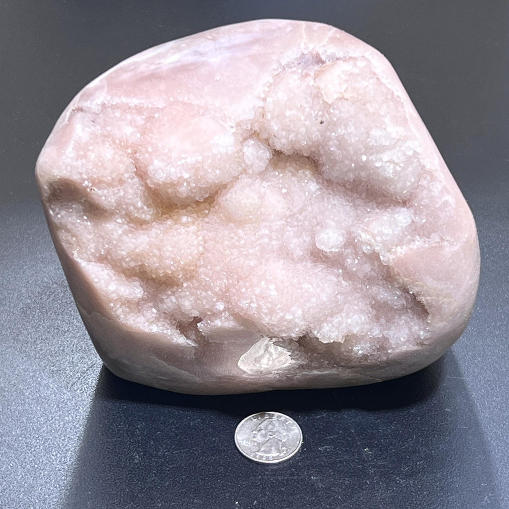 Pink amethyst druzy freeform standing on a dark surface with a quarter in front for scale