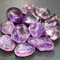 Polished amethyst tumbled stones in lavender and deep purple with rounded shapes on a dark textured surface.