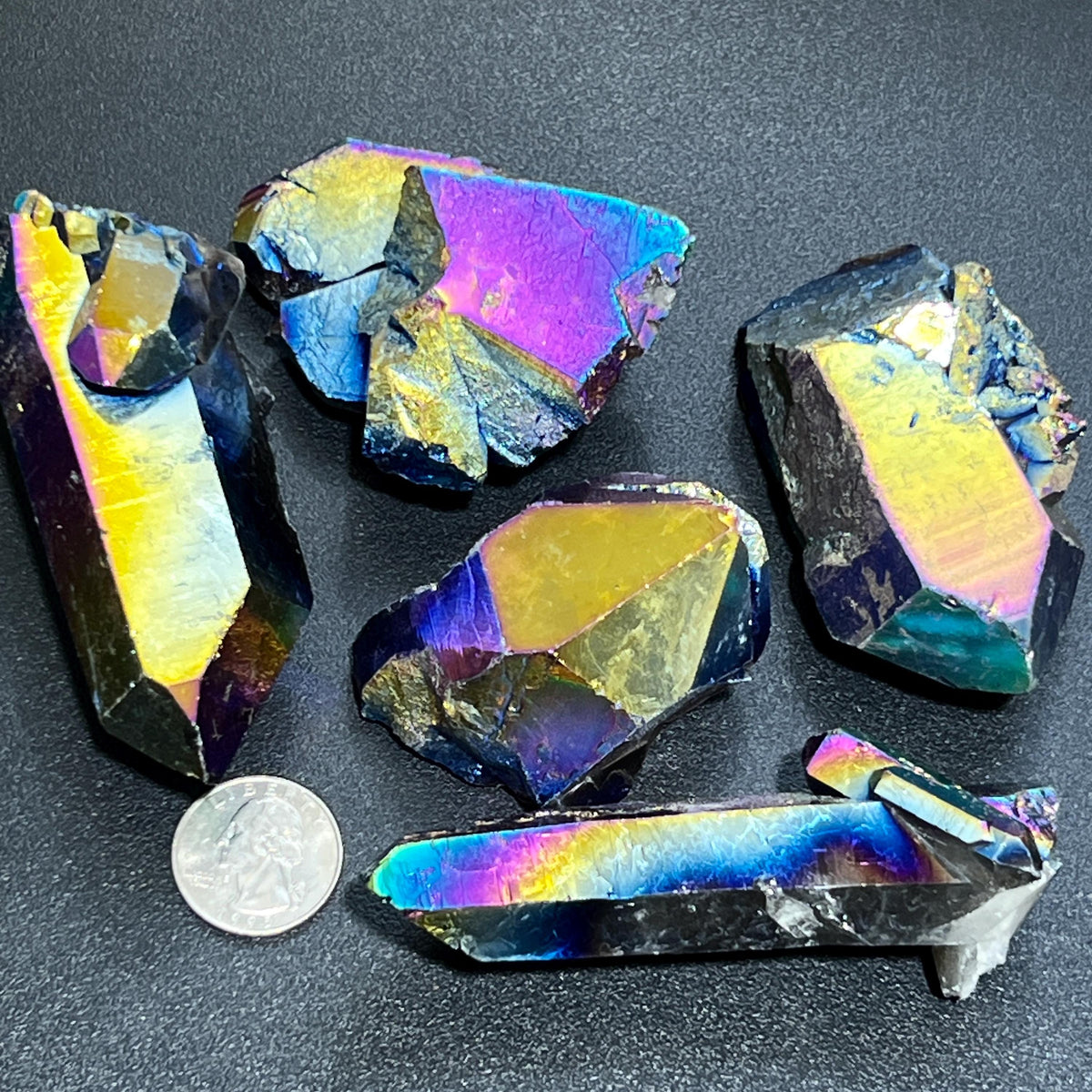 Rainbow-finished titanium aura quartz clusters and rough points beside a quarter for size comparison.
