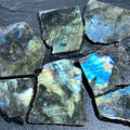 Rough-cut labradorite slabs with polished faces showing blue, green and gold flashes on a dark textured surface