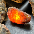 Rough black amber piece glowing orange and yellow when backlit, surrounded by dark resin pieces