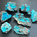 Rough chrysocolla clusters with bright turquoise-blue rounded surfaces on dark gray matrix arranged on a black background