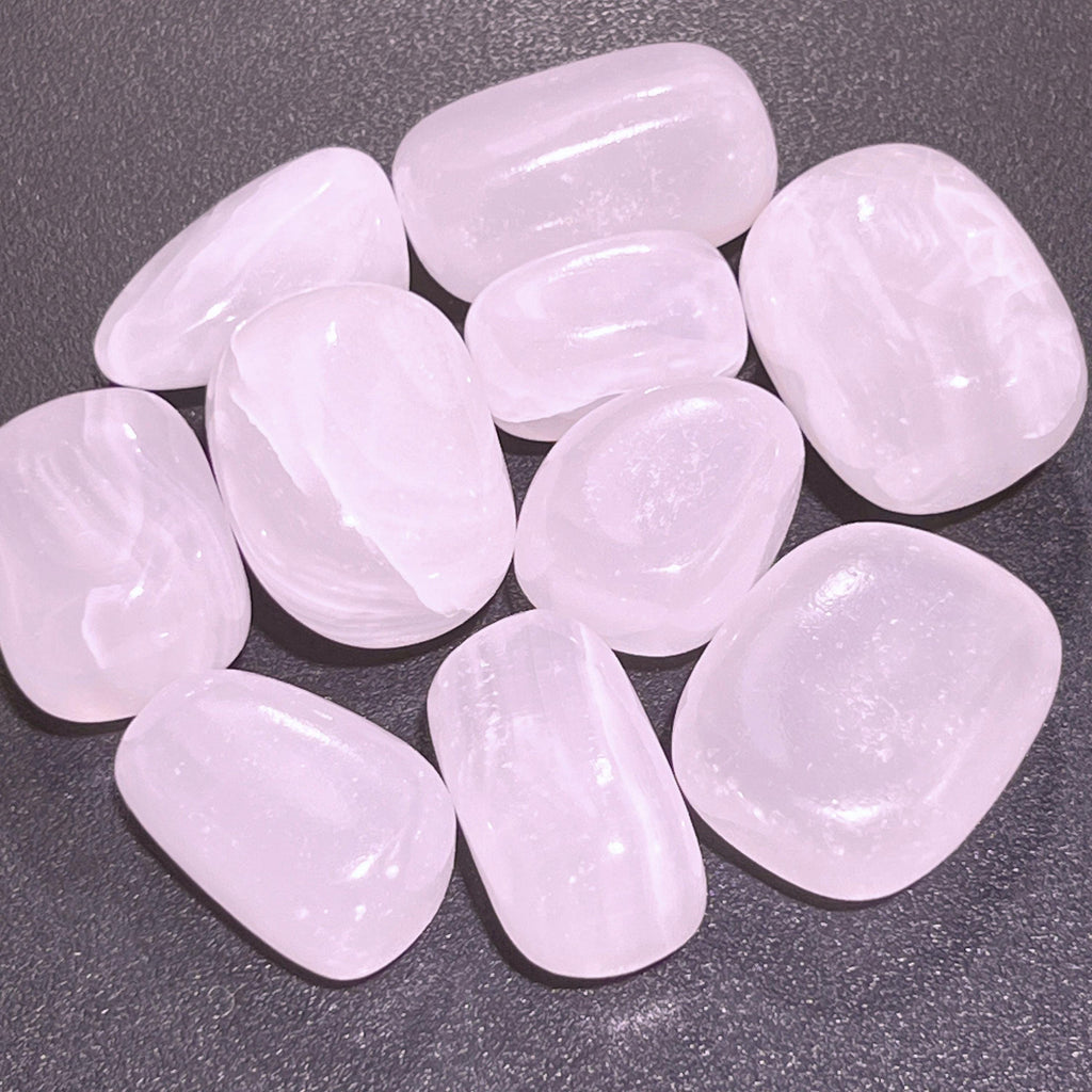 Rounded pink mangano calcite tumbled stones with pale banding arranged on a dark textured surface.