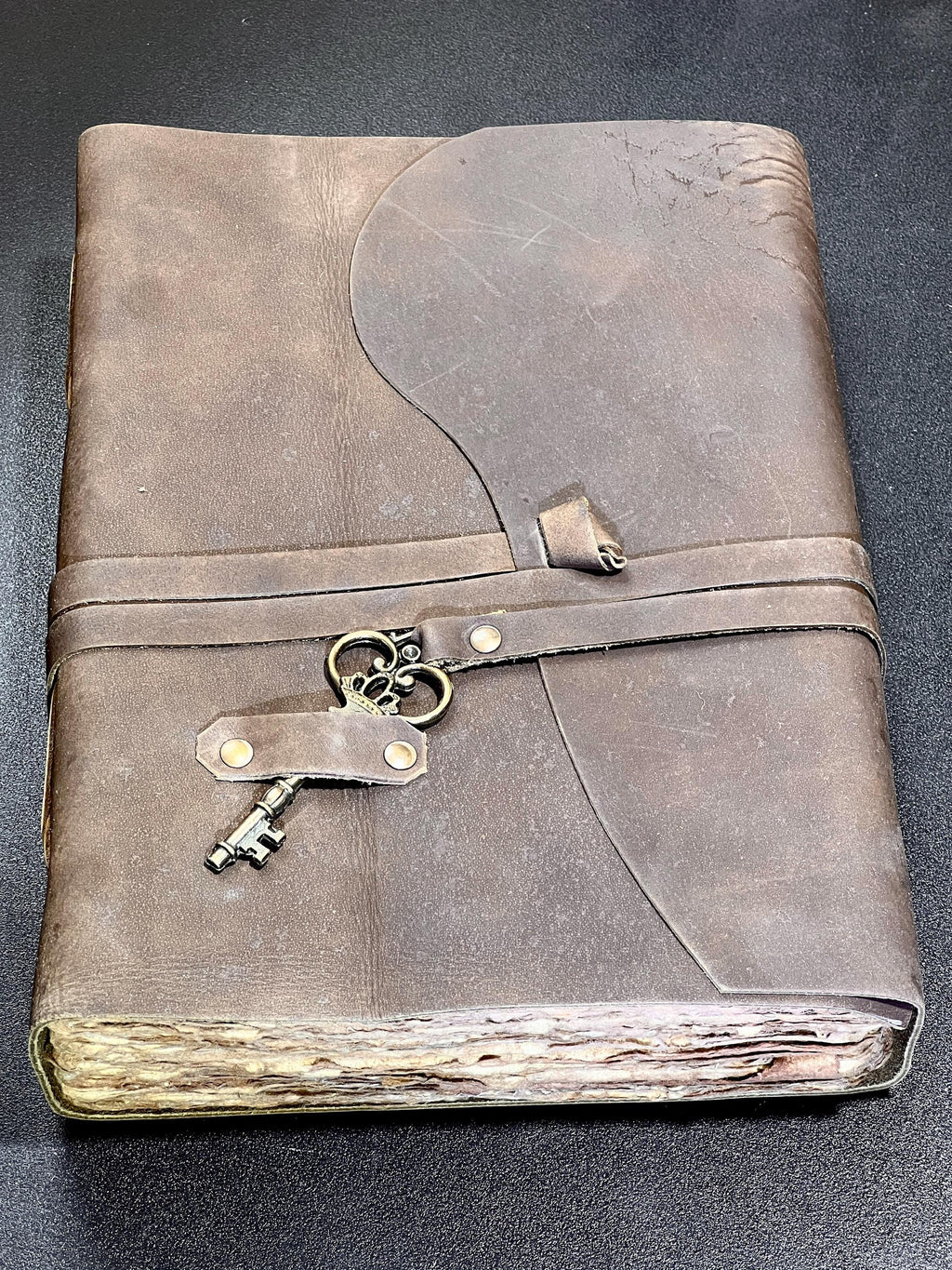 Rustic brown leather-bound notebook with wraparound strap, decorative metal key and uneven cream page edges