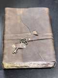 Rustic brown leather-bound notebook with wraparound strap, decorative metal key and uneven cream page edges
