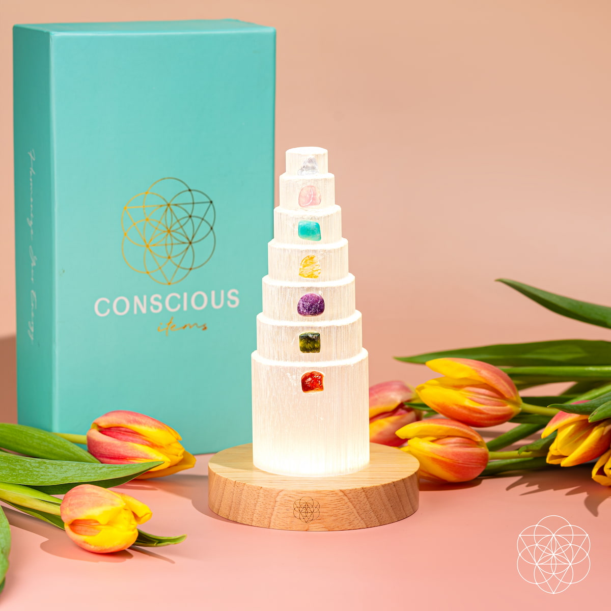 Selenite crystal lamp beside a turquoise Conscious Items box and yellow tulips on a peach background.
I